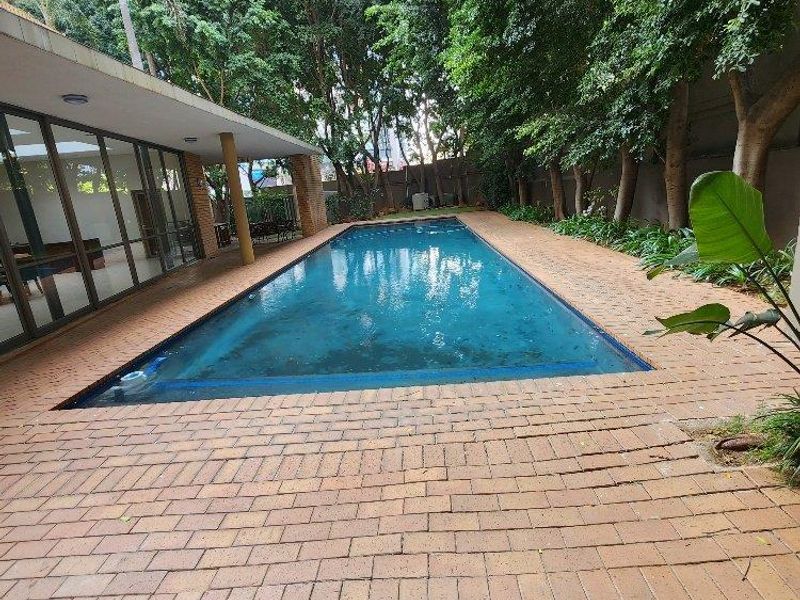Outdoor pool area featuring a rectangular swimming pool, brick paved surround, and a covered patio area with large sliding glass doors.