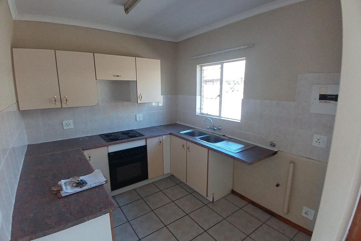 A functional kitchen featuring built-in cabinetry, laminate countertops, an electric hob, oven, and double sink with tiled flooring and splashbacks.