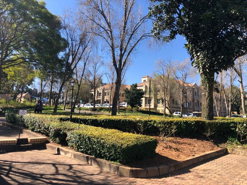 A view of the office property exterior featuring landscaped gardens, paved walkways, and mature trees surrounding the building facade.