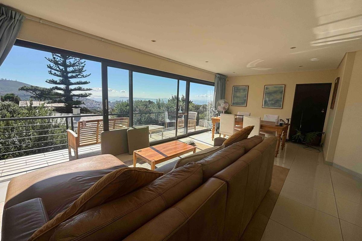 Spacious open-plan living and dining area featuring large sliding glass doors that open onto a balcony with scenic coastal views.