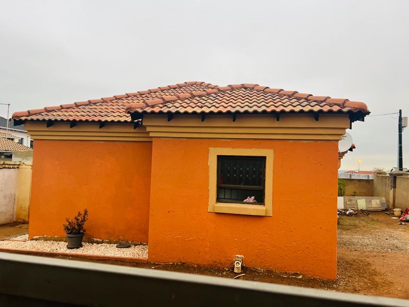 Rear view of the house featuring terracotta roof tiles, orange plastered walls, and security bars on the window.