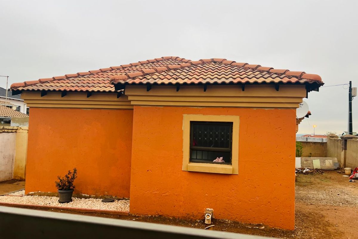 Rear view of the house featuring terracotta roof tiles, orange plastered walls, and security bars on the window.