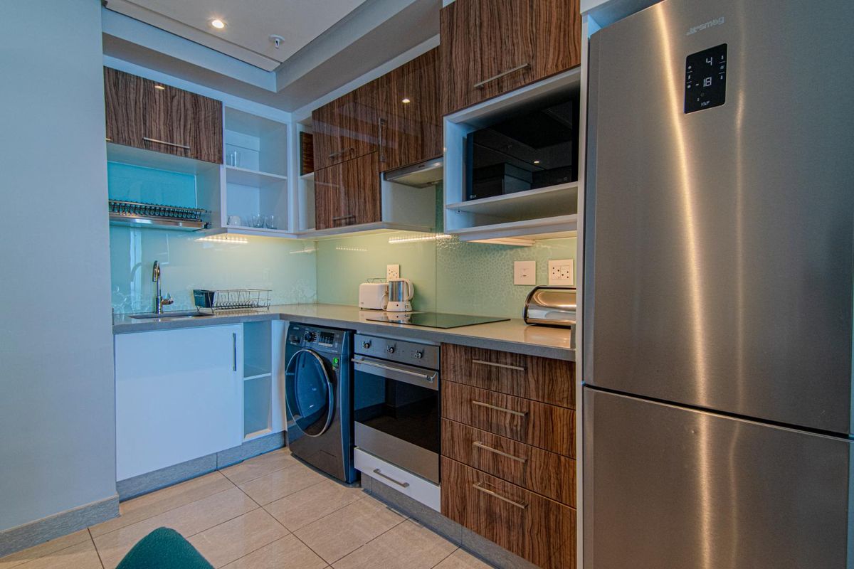 Modern kitchen featuring wood-grain cabinetry, stone countertops, glass splashback, integrated oven, hob, extractor fan, and built-in laundry appliance space.
