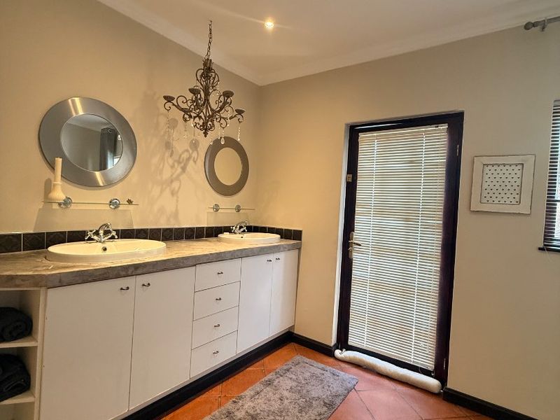 A bathroom featuring a double vanity with built-in cabinetry, tiled countertop, and direct access to an outdoor area through a glass door.