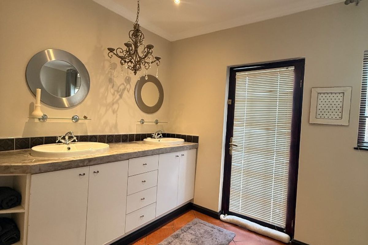 A bathroom featuring a double vanity with built-in cabinetry, tiled countertop, and direct access to an outdoor area through a glass door.
