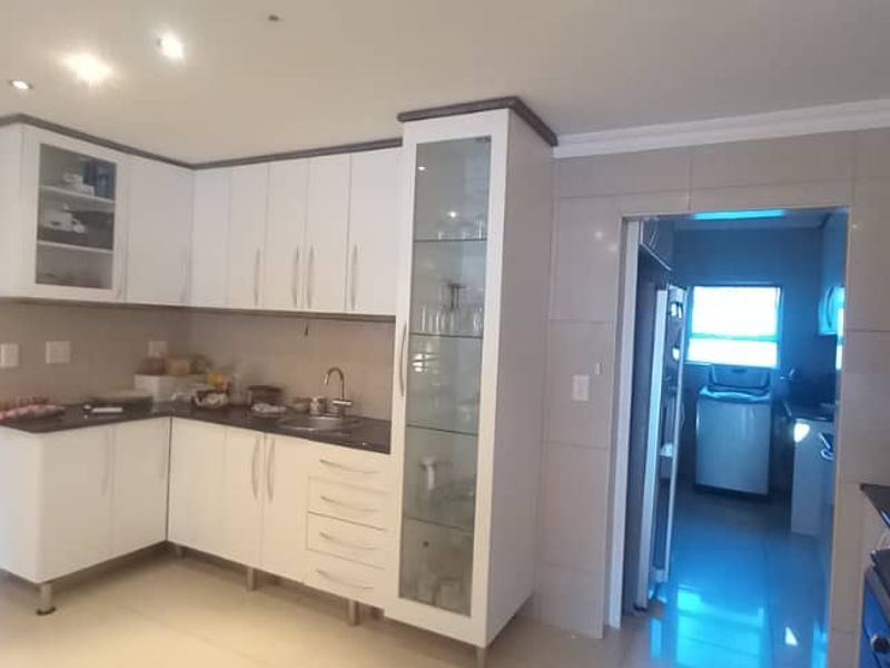 Modern kitchen featuring white cabinetry, glass-front display units, dark countertops, and a tiled splashback, with an adjacent scullery area visible.