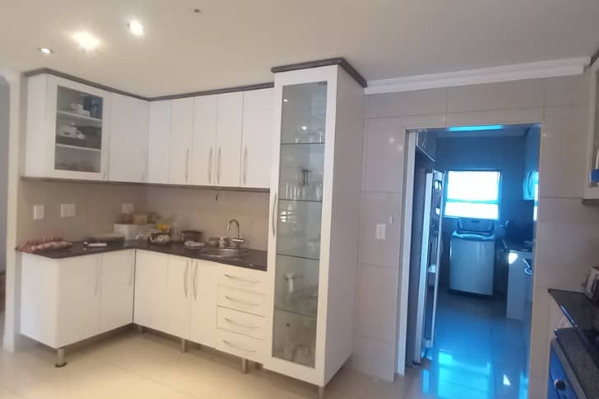 Modern kitchen featuring white cabinetry, glass-front display units, dark countertops, and a tiled splashback, with an adjacent scullery area visible.