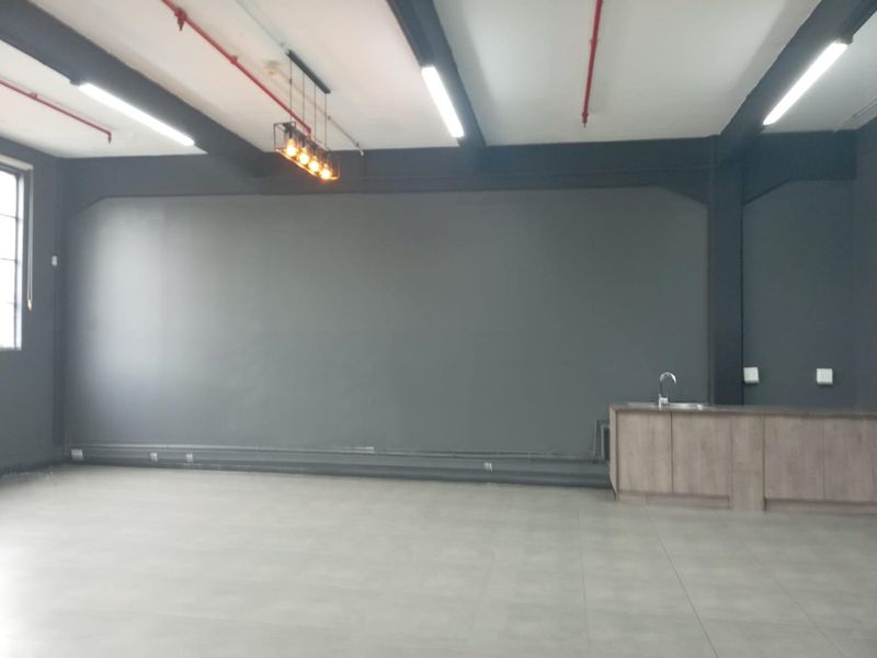 Spacious open-plan office area featuring industrial-style exposed ceilings, tiled flooring, and a convenient kitchenette unit with a sink.