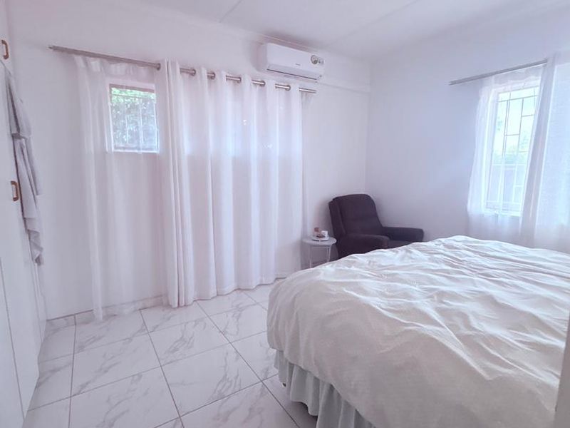 A bright bedroom featuring marble-look floor tiles, built-in cupboards, and a wall-mounted split-system air conditioner.