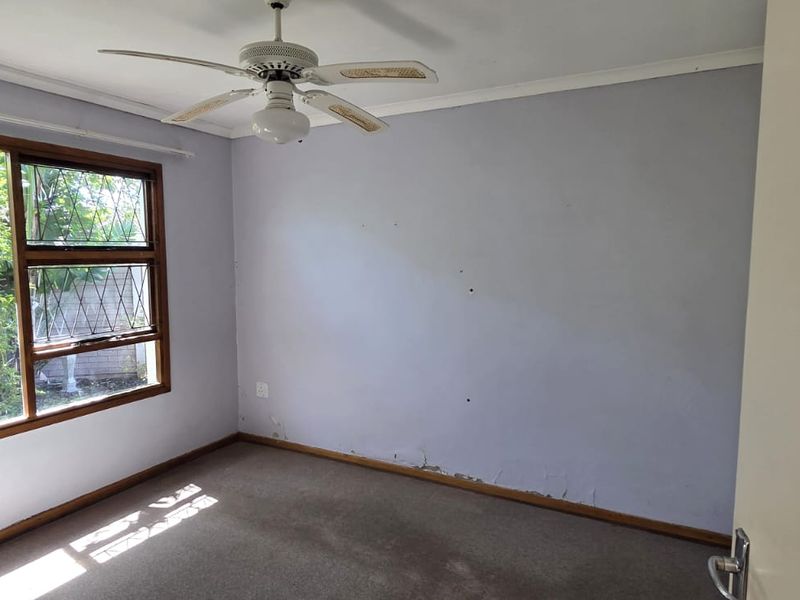 An empty bedroom featuring a ceiling fan, carpeted flooring, and a large leaded glass window with visible wall surface damage.