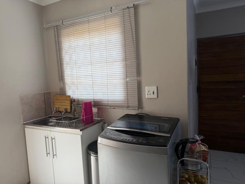 A functional laundry area featuring a stainless steel sink, built-in cabinetry, and dedicated space for a washing machine.