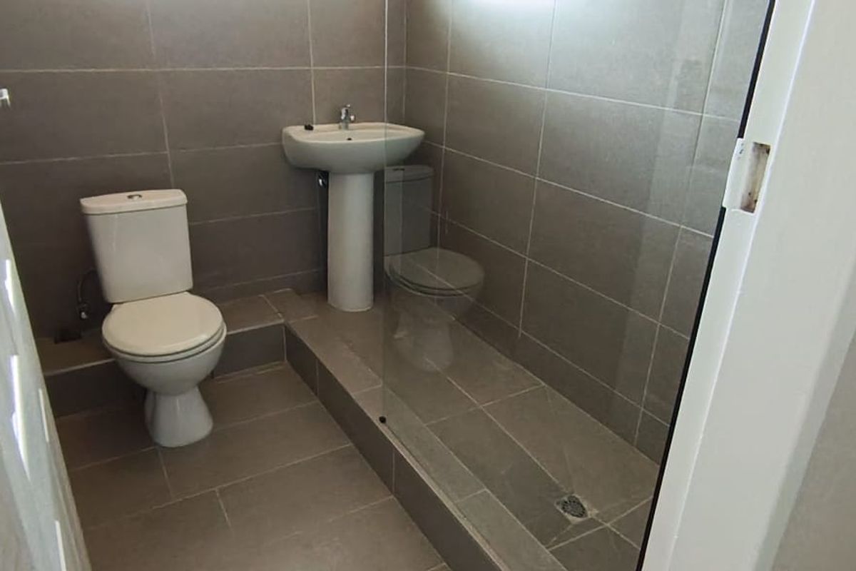 A compact bathroom featuring tiled walls and flooring, a pedestal basin, a toilet, and a walk-in shower area with a glass screen.