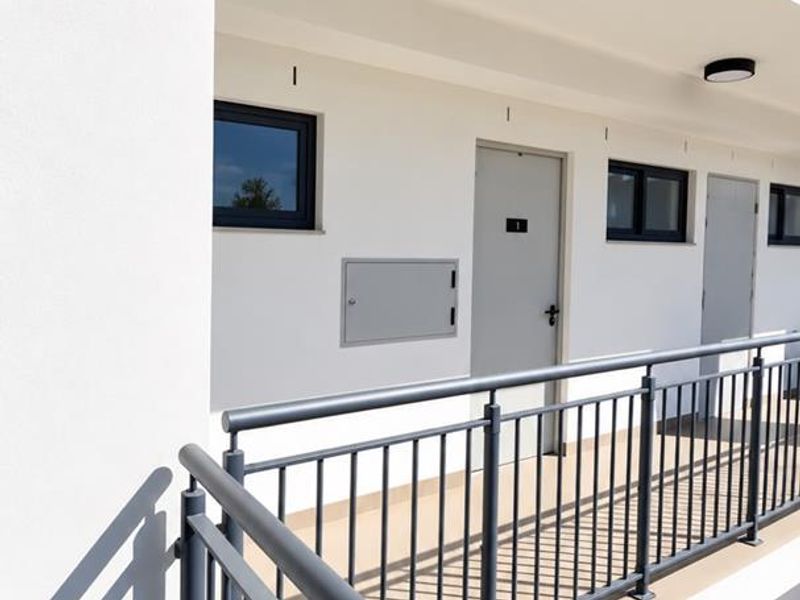 A clean, modern exterior apartment walkway featuring metal safety railings, neutral wall finishes, and secure access doors.