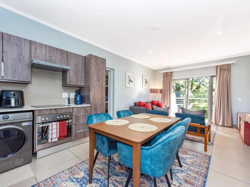 An open-plan living and kitchen area featuring modern wood-finish cabinetry, integrated appliances, tiled floors, and a sliding door leading to an outdoor balcony.