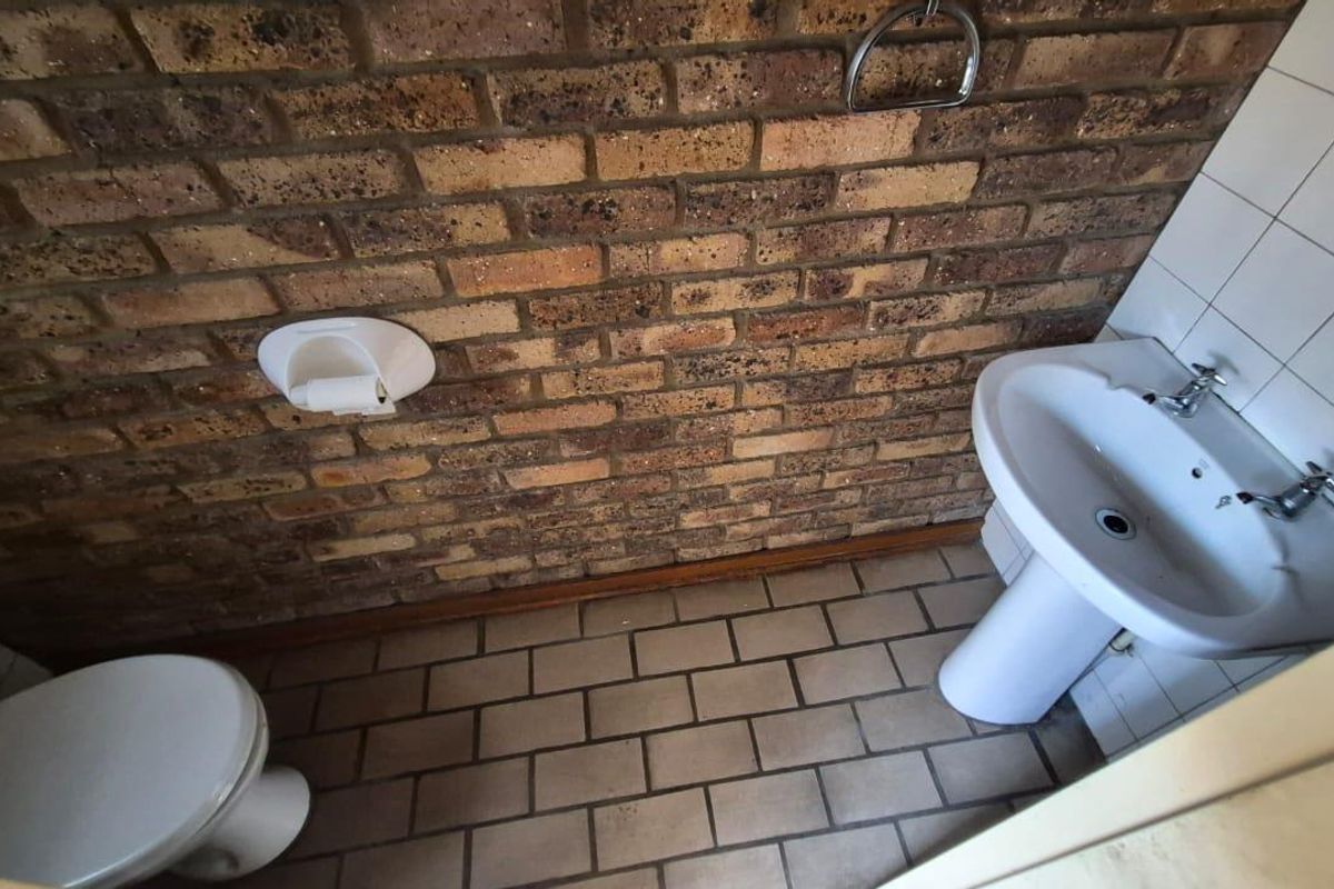 A compact bathroom featuring an exposed brick wall, pedestal basin, and tiled flooring, presenting an opportunity for modernization.