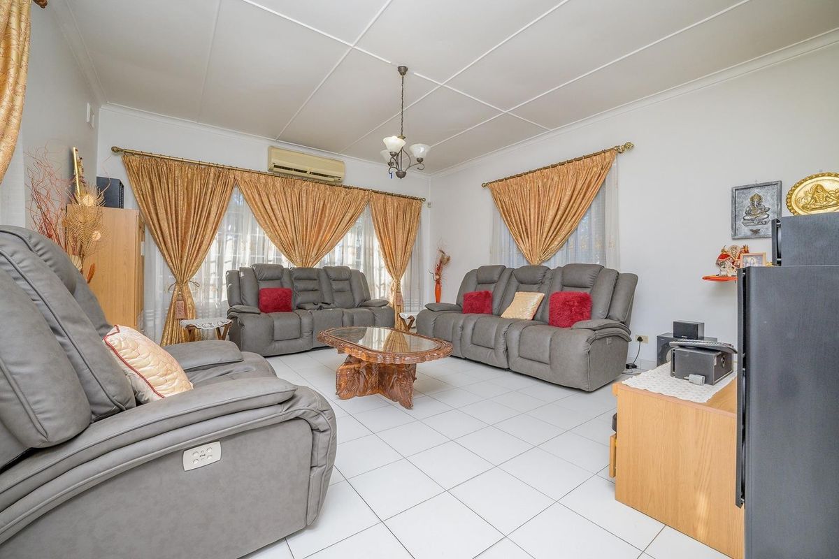 A spacious living room featuring white tiled flooring, a split-system air conditioner, and a classic grid-pattern ceiling.