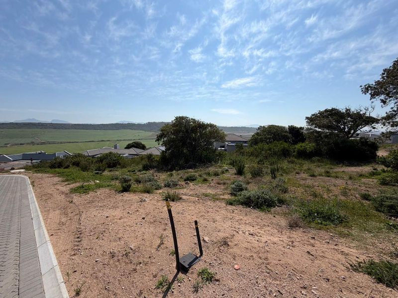 A vacant residential plot featuring a paved driveway edge, utility connection point, and expansive views over the surrounding landscape.