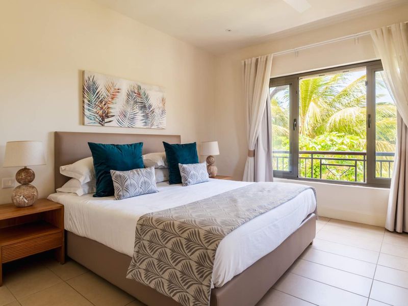 A well-maintained bedroom featuring tiled flooring, neutral walls, and a large window with access to a balcony, providing natural light and garden views.