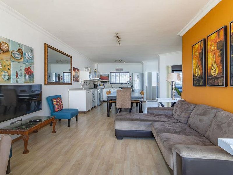 Spacious open-plan living and dining area featuring laminate flooring and a functional kitchen layout, offering a versatile space for modern apartment living.