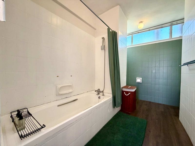 A dated bathroom featuring a built-in bathtub with shower mixer, tiled wall finishes, and a high-level window providing natural light.