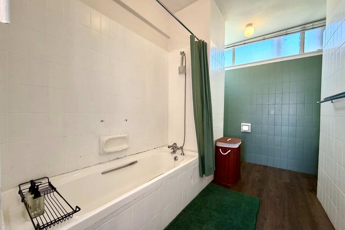 A dated bathroom featuring a built-in bathtub with shower mixer, tiled wall finishes, and a high-level window providing natural light.