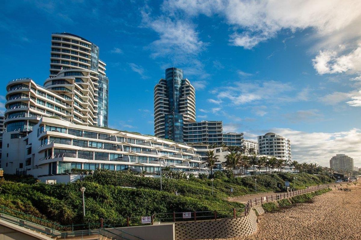 A scenic exterior view of a modern apartment complex situated along the coastline, featuring tiered balconies and contemporary architectural design.