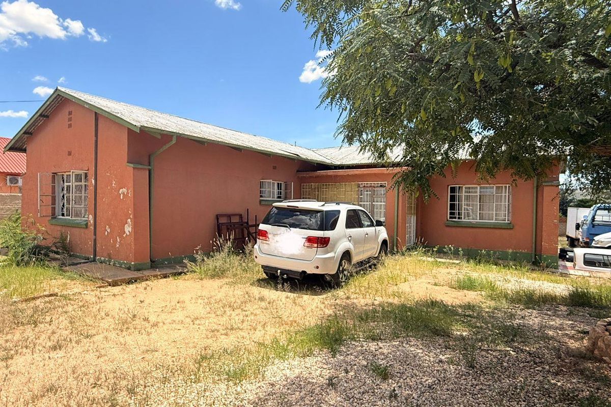 Front elevation of a single-story house featuring a corrugated metal roof, steel-framed windows, and masonry walls requiring exterior maintenance and landscaping.