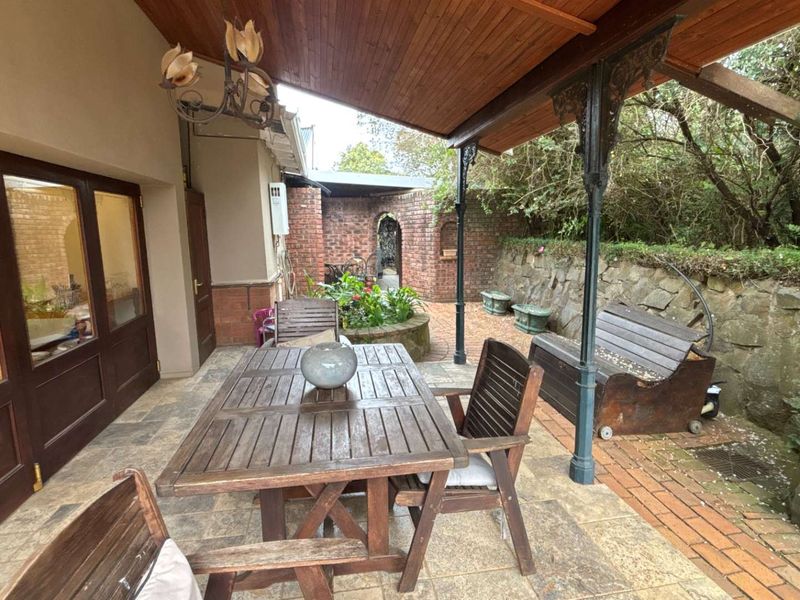A covered patio area featuring a timber ceiling, wrought iron columns, and a combination of stone and brick paving, adjacent to a stone retaining wall.
