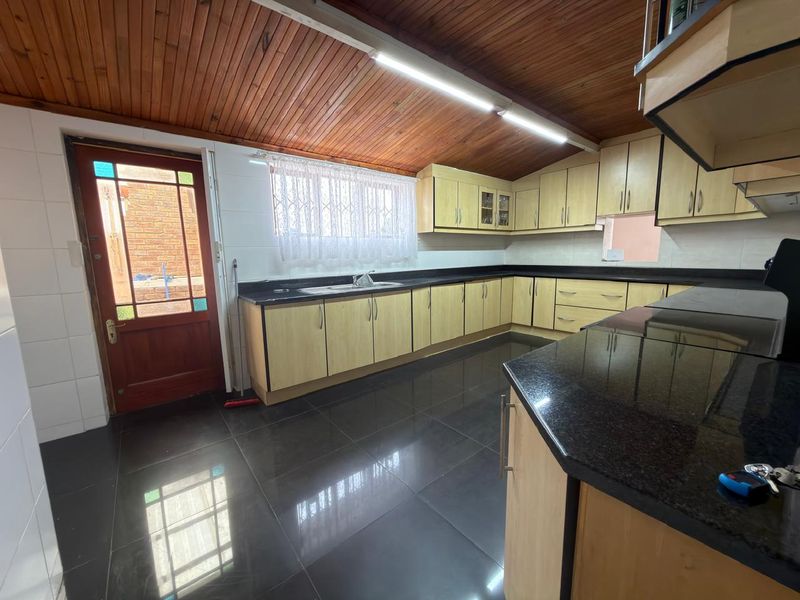 Spacious kitchen featuring light wood cabinetry, dark granite countertops, tiled flooring, and a distinctive timber ceiling with direct access to the exterior.