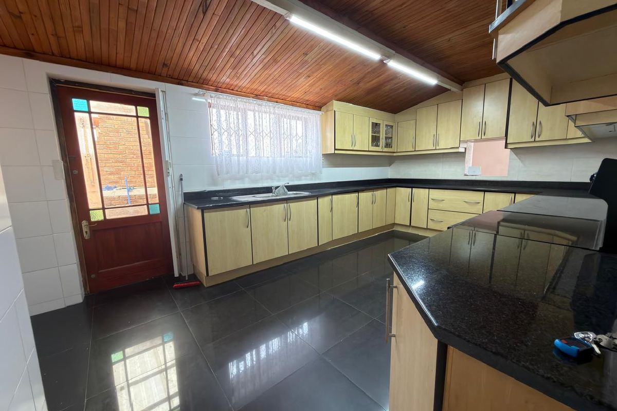 Spacious kitchen featuring light wood cabinetry, dark granite countertops, tiled flooring, and a distinctive timber ceiling with direct access to the exterior.