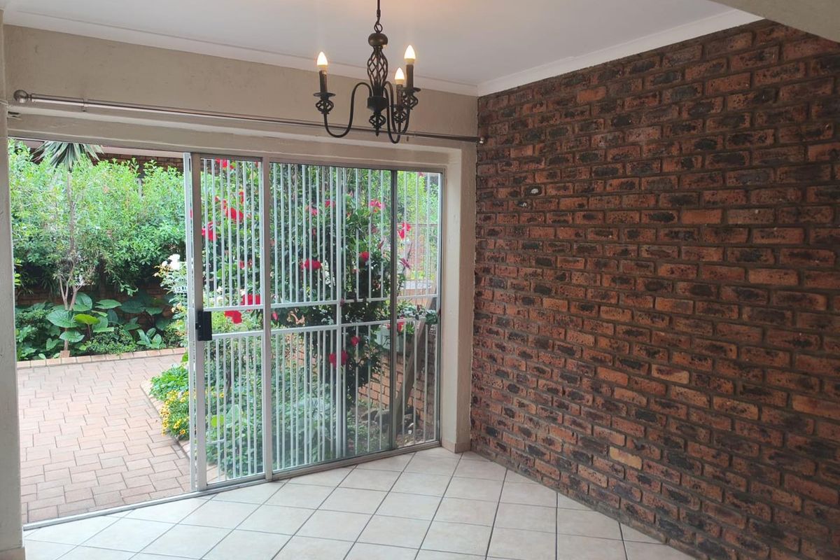 A bright living area featuring a rustic exposed brick feature wall, tiled flooring, and sliding glass doors opening onto a paved garden patio.