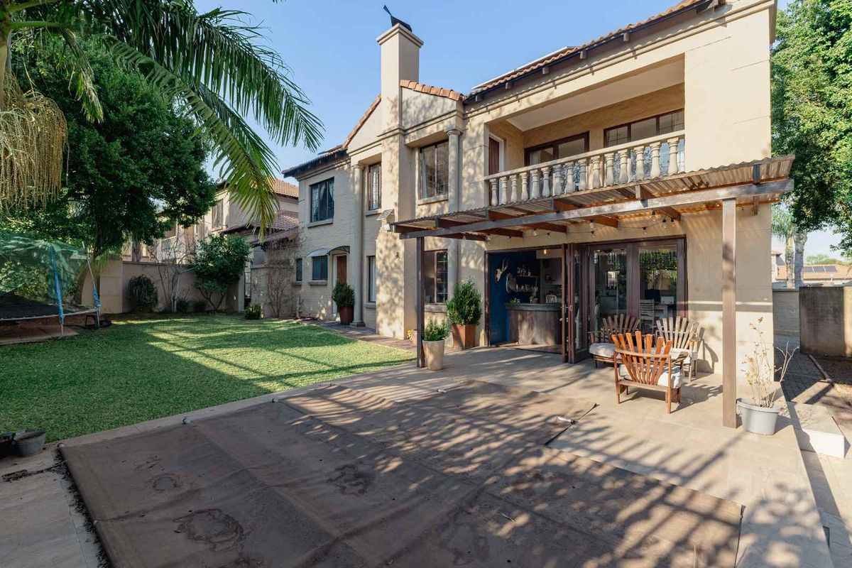 Rear view of the townhouse featuring a covered patio, upper balcony with balustrade, and a private garden with a swimming pool cover.