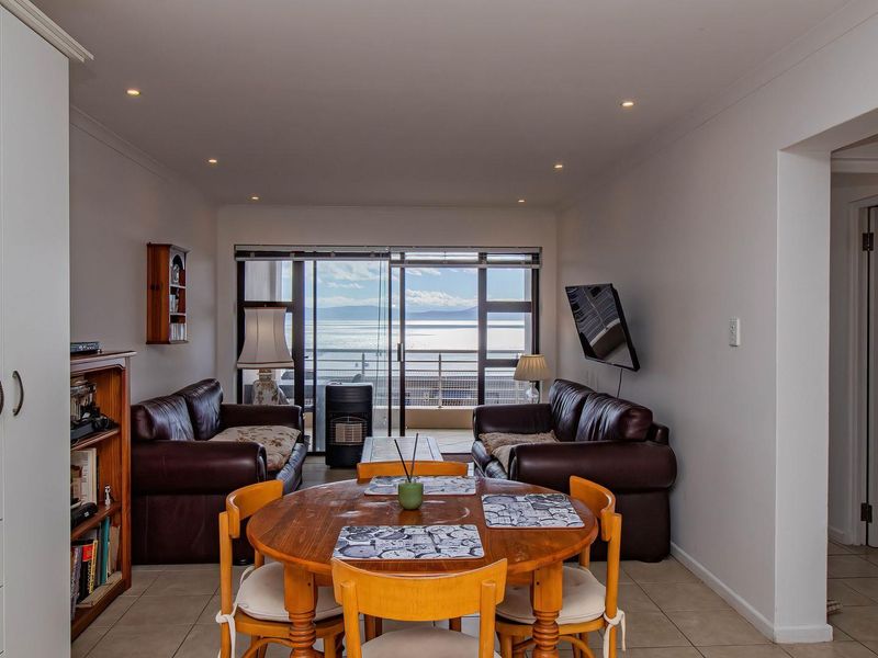 Open-plan living and dining area featuring tiled floors, recessed lighting, and sliding glass doors leading to a balcony with scenic water views.