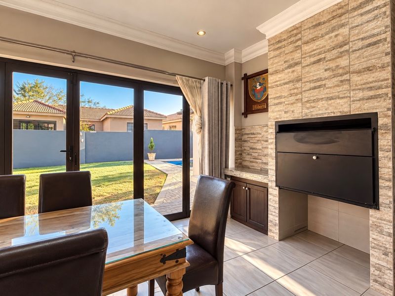 A well-maintained living area featuring a built-in braai with stone cladding, tiled floors, and large sliding doors opening to the garden and pool area.