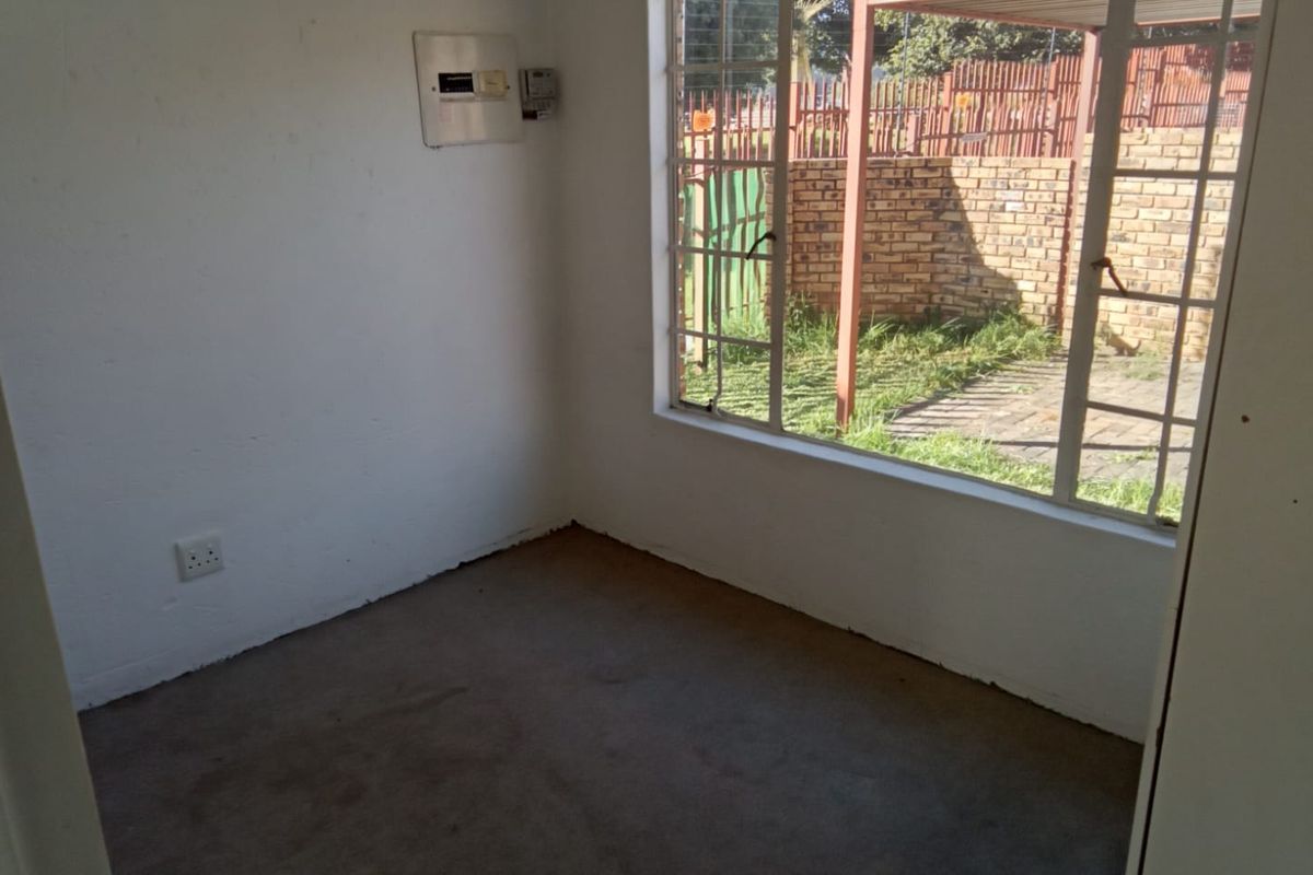 A small, empty room featuring a large window overlooking the rear garden, carpeted flooring, and a wall-mounted electrical distribution board.