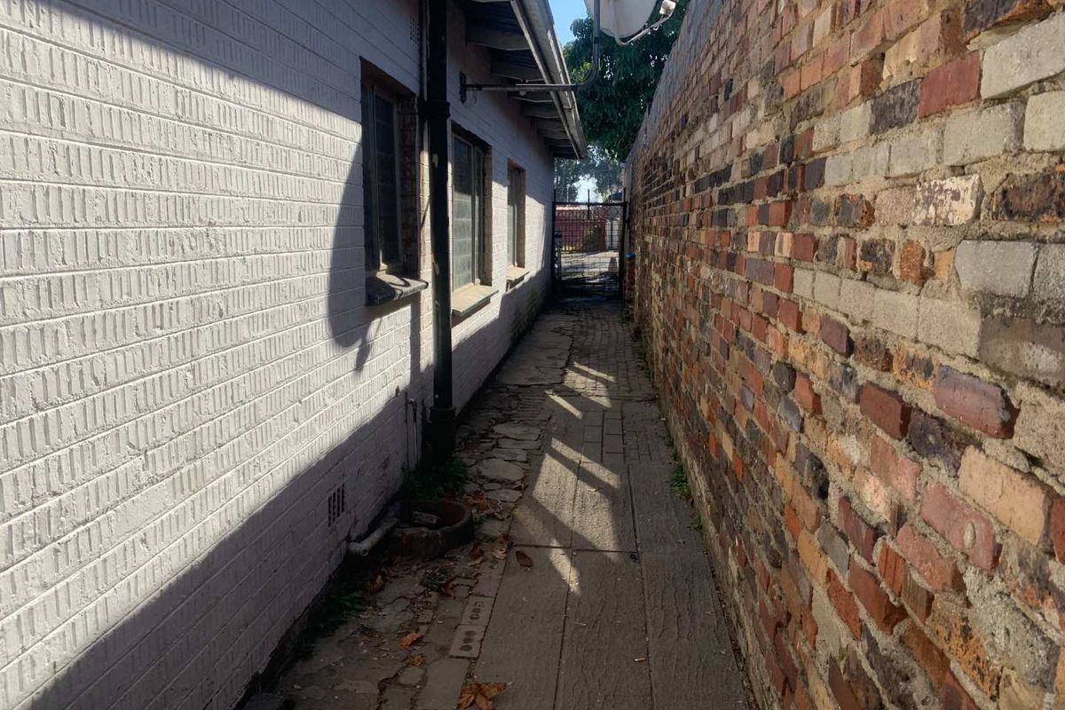 A narrow side passage featuring a paved walkway between the main house structure and a boundary brick wall.