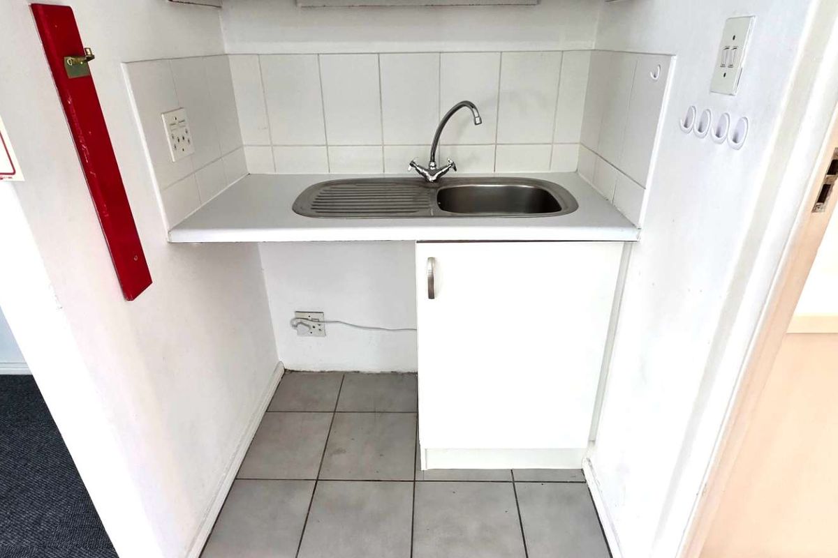 A compact kitchenette area featuring a stainless steel sink, tiled splashback, and a single base cabinet for storage.