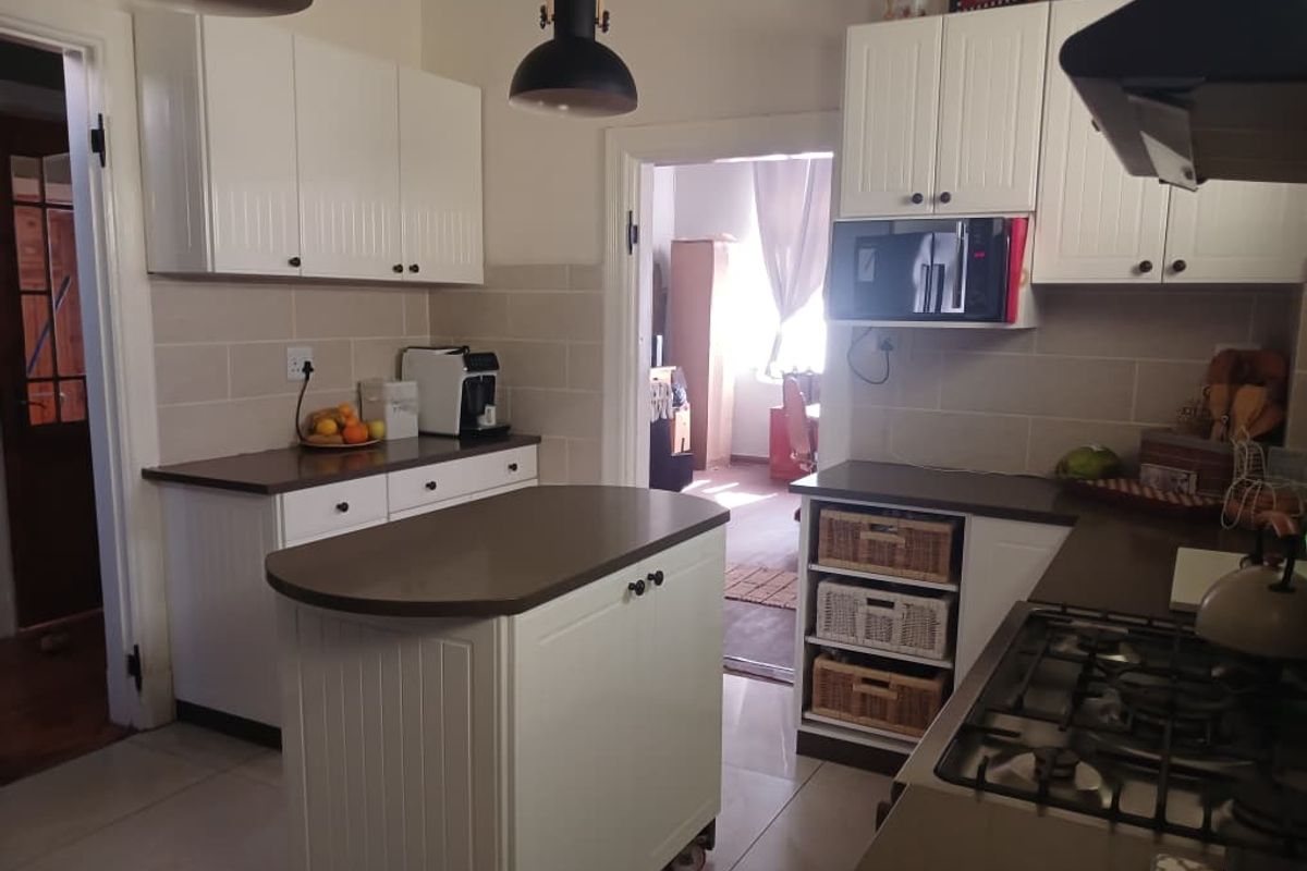 A functional kitchen featuring white cabinetry, a central island, gas hob, extractor fan, and tiled finishes, providing a clean and practical cooking space.