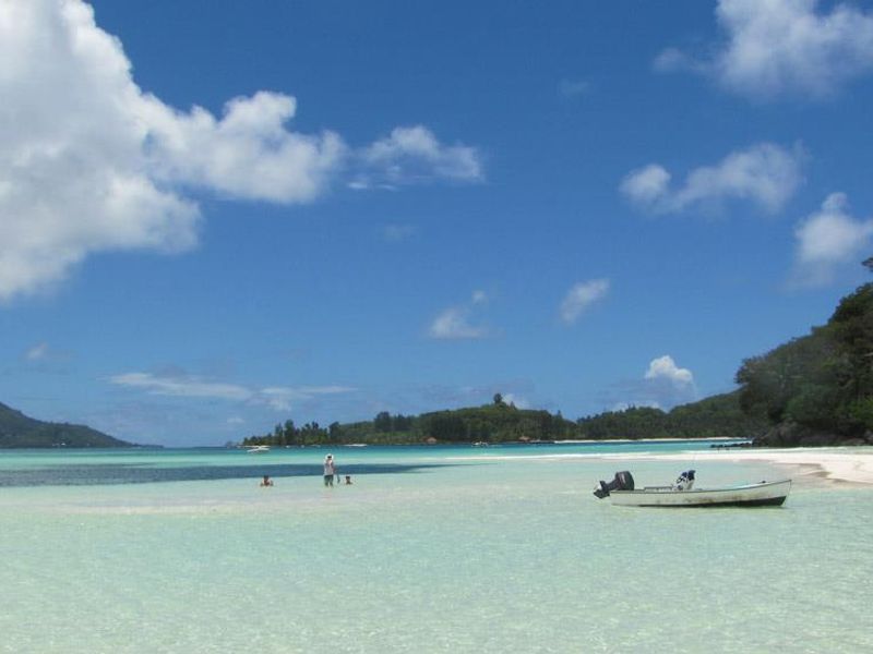 A scenic view of a tropical beach with clear turquoise water, white sand, and distant islands.