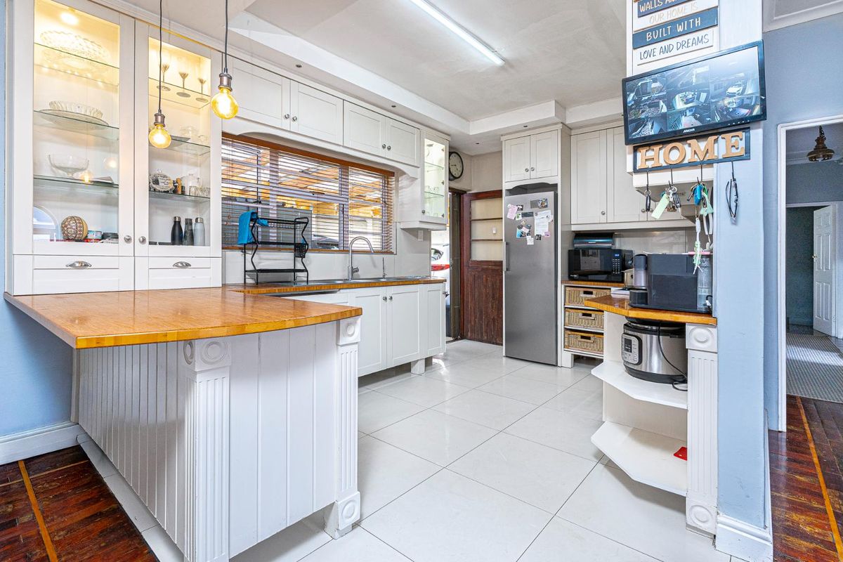 A well-maintained kitchen featuring white built-in cabinetry, wooden countertops, tiled flooring, and integrated display shelving with glass-fronted cabinets.