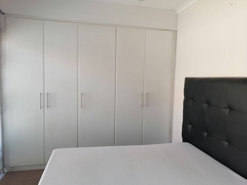 A bedroom featuring floor-to-ceiling built-in cupboards with modern handles and clean white finishes.