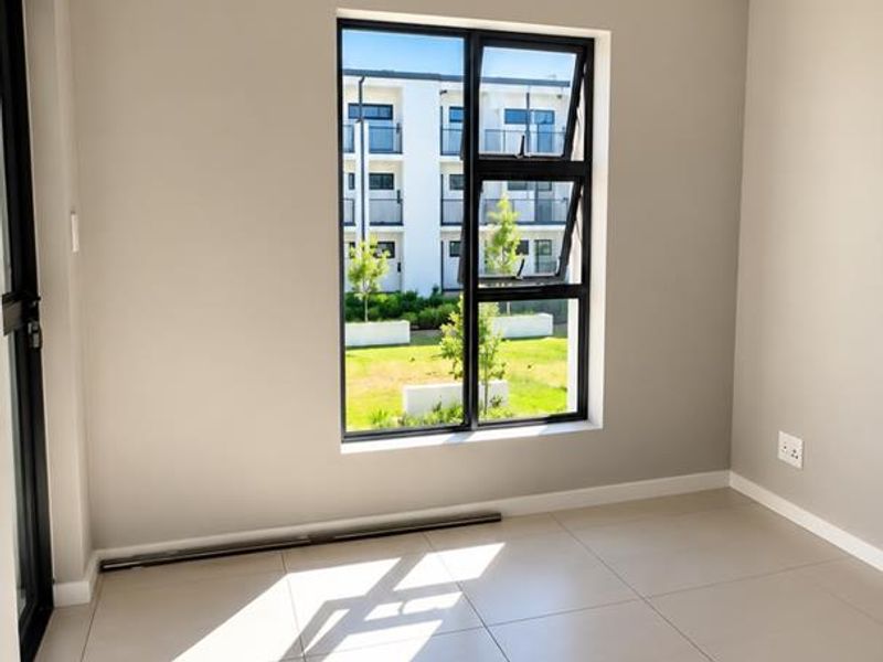 A bright, empty bedroom featuring neutral tiled flooring, modern aluminium window frames, and clean finishes, ready for personalization.