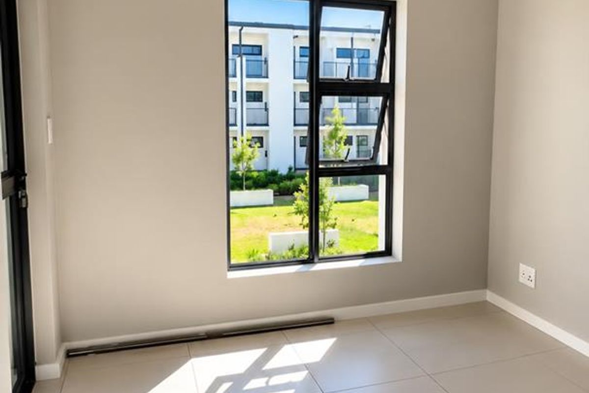 A bright, empty bedroom featuring neutral tiled flooring, modern aluminium window frames, and clean finishes, ready for personalization.