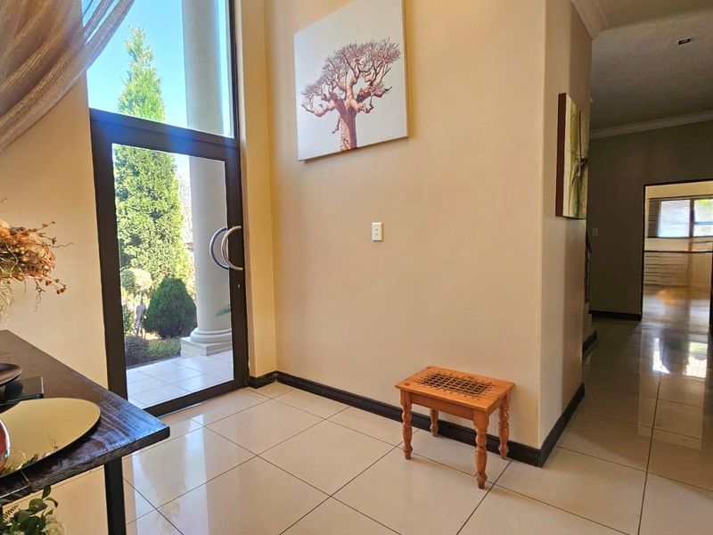 Bright entrance foyer featuring large glass door, polished tiled flooring, and neutral wall finishes leading into the home's hallway.