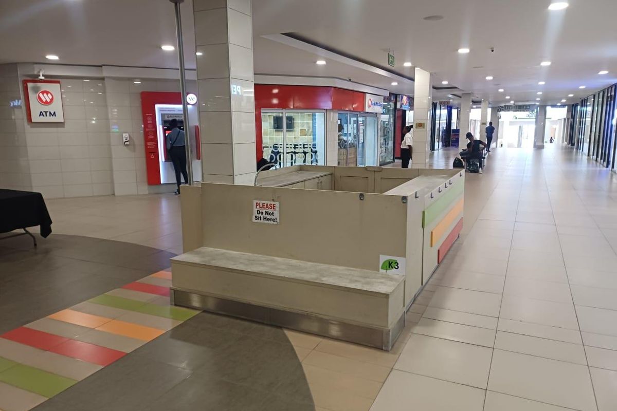 A view of a retail shopping centre hallway featuring a central kiosk, tiled flooring, recessed lighting, and an integrated ATM facility.