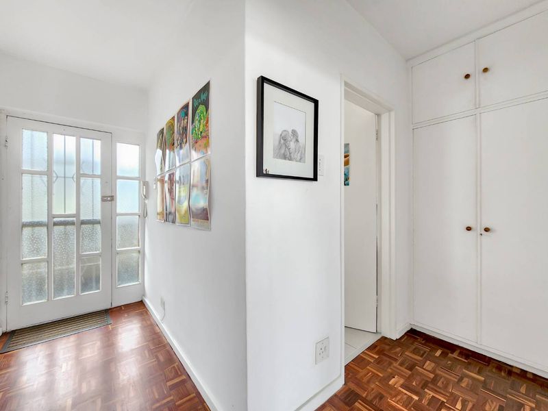 Bright entrance hall featuring classic parquet flooring, a glass-panelled front door, and ample built-in storage cupboards.