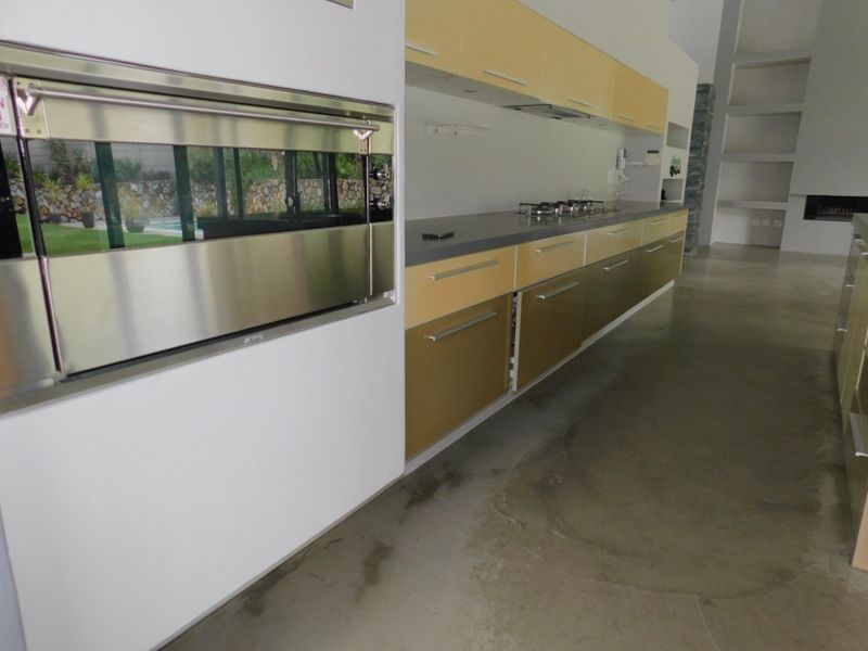 Modern kitchen featuring polished concrete floors, built-in stainless steel oven, gas cooktop, and sleek two-tone cabinetry with stone countertops.