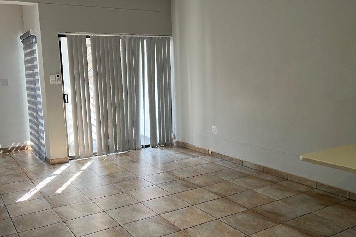 An empty living area featuring tiled flooring, vertical blinds, and access to an outdoor space.