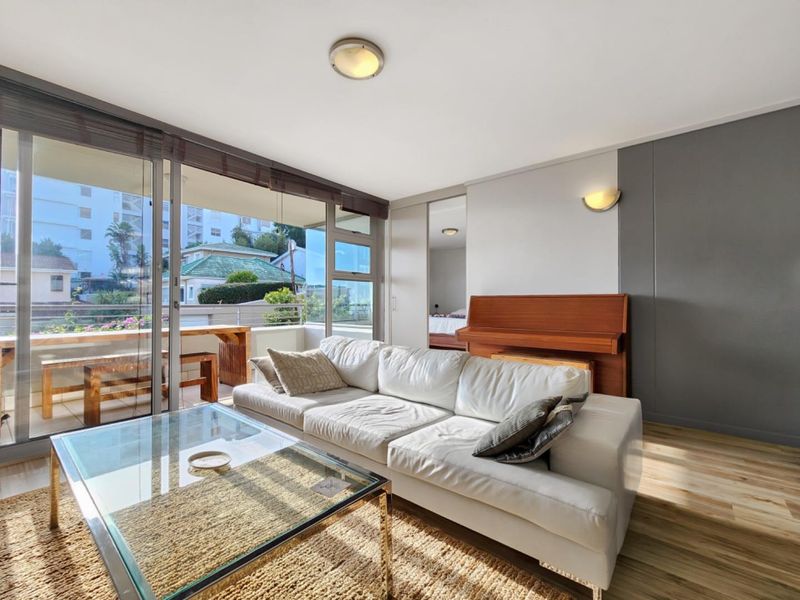 Bright living room featuring laminate flooring, modern wall sconces, and large sliding glass doors that open onto a private balcony.