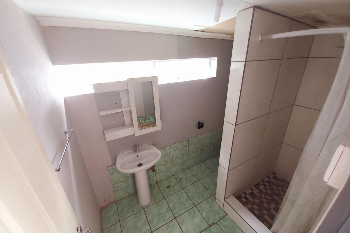 A dated bathroom featuring a pedestal basin, tiled shower enclosure, and horizontal clerestory window, requiring significant maintenance and cosmetic updates.
